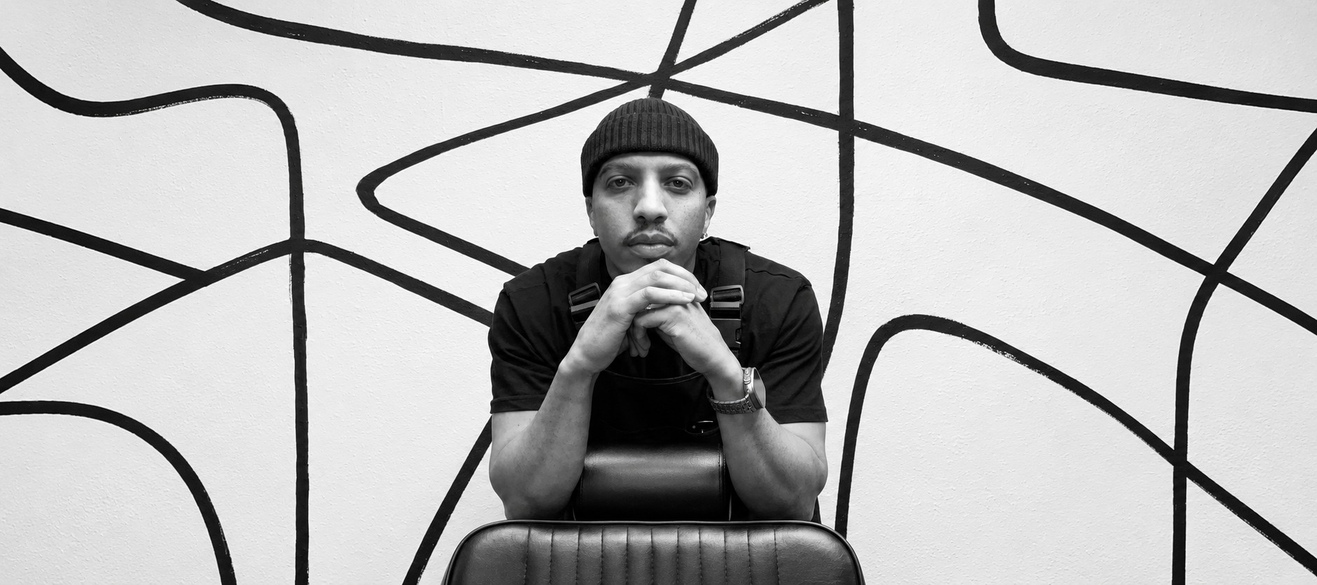 Samuel C. Shears seated behind a barber chair against a black-and-white mural.